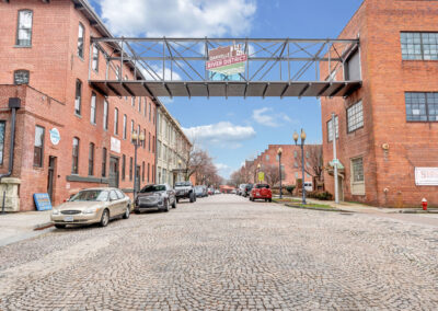 Third-story metal bridge between two brick industrial buildings going over cobblestoned streets with "Danville Historic River District" sign affixed to bridge