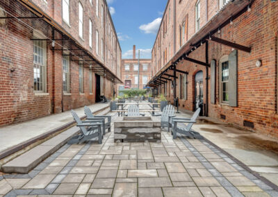 Narrow patio courtyard with industrial brick buildings on each side, chairs and fire pits in the center