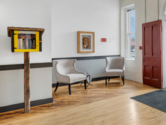 Entryway with two chairs, heavy red barn door and little free library stand