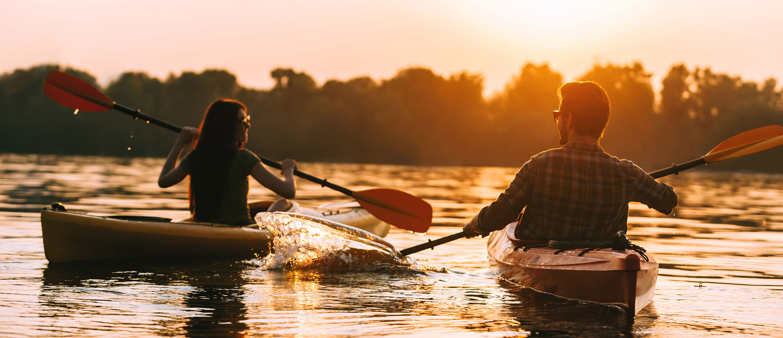 Couple paddling on river in kayaks at sunset