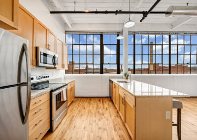 Apartment kitchen with large industrial windows, stainless steel appliances, and tall ceilings