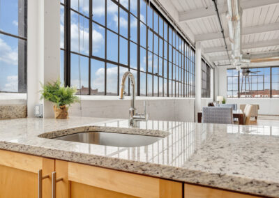 Close up of granite counter tops with open floor plan apartment in the background and large industrial windows